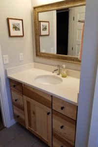 A chestnut bathroom sink cabinet with granite counter and a large mirror.