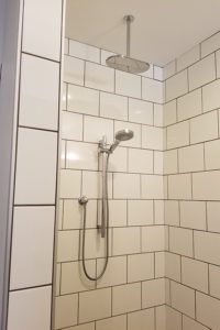 A tiled shower with detachable shower head and tile walls.
