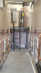 A long room with a water heater and various copper and PVC piping.