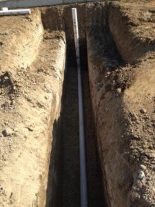 A PVC pipe laid in a long trench in the ground.