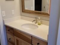 A chestnut bathroom sink cabinet with granite counter and a large mirror.