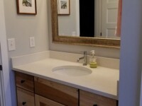 A chestnut bathroom sink cabinet with granite counter and a large mirror.