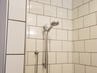 A tiled shower with detachable shower head and tile walls.