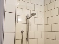 A tiled shower with detachable shower head and tile walls.