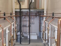 A long room with a water heater and various copper and PVC piping.